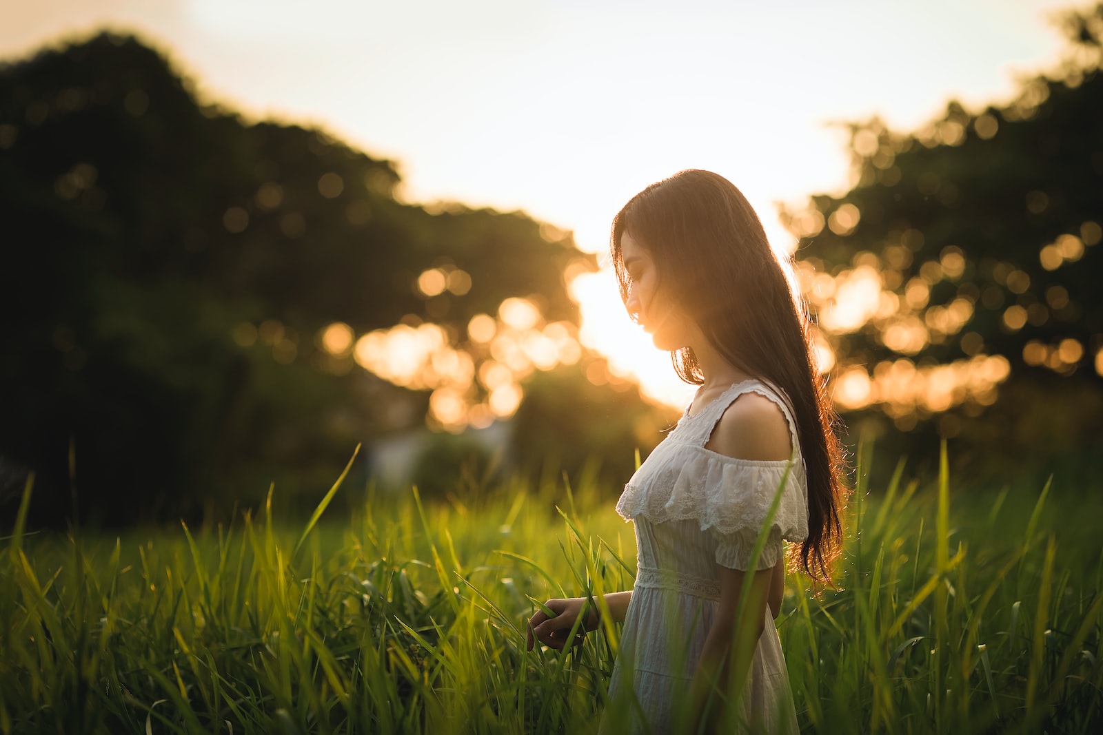 shallow focus photography of woman standing on grass field while holding grass